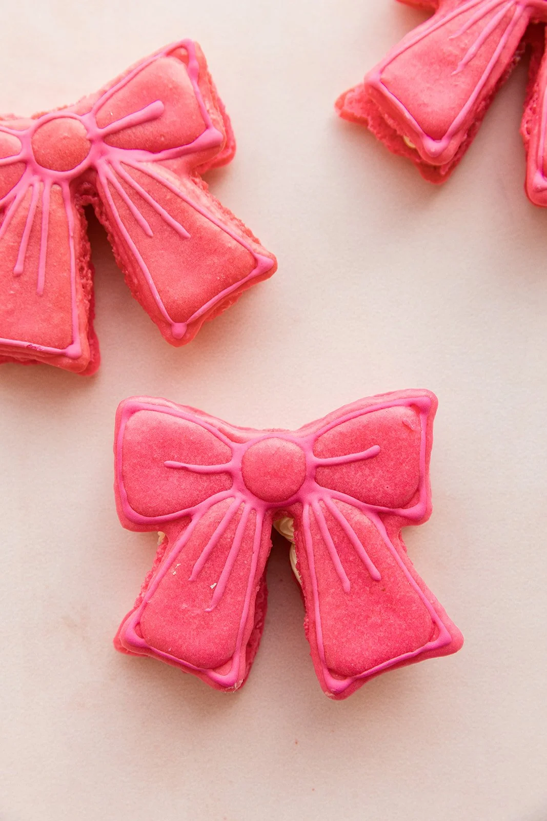 Pink bow-shaped macaron cookies decorated with icing, arranged on a white surface — handcrafted macarons and desserts at Decadent Macaron café in Gilbert, Arizona