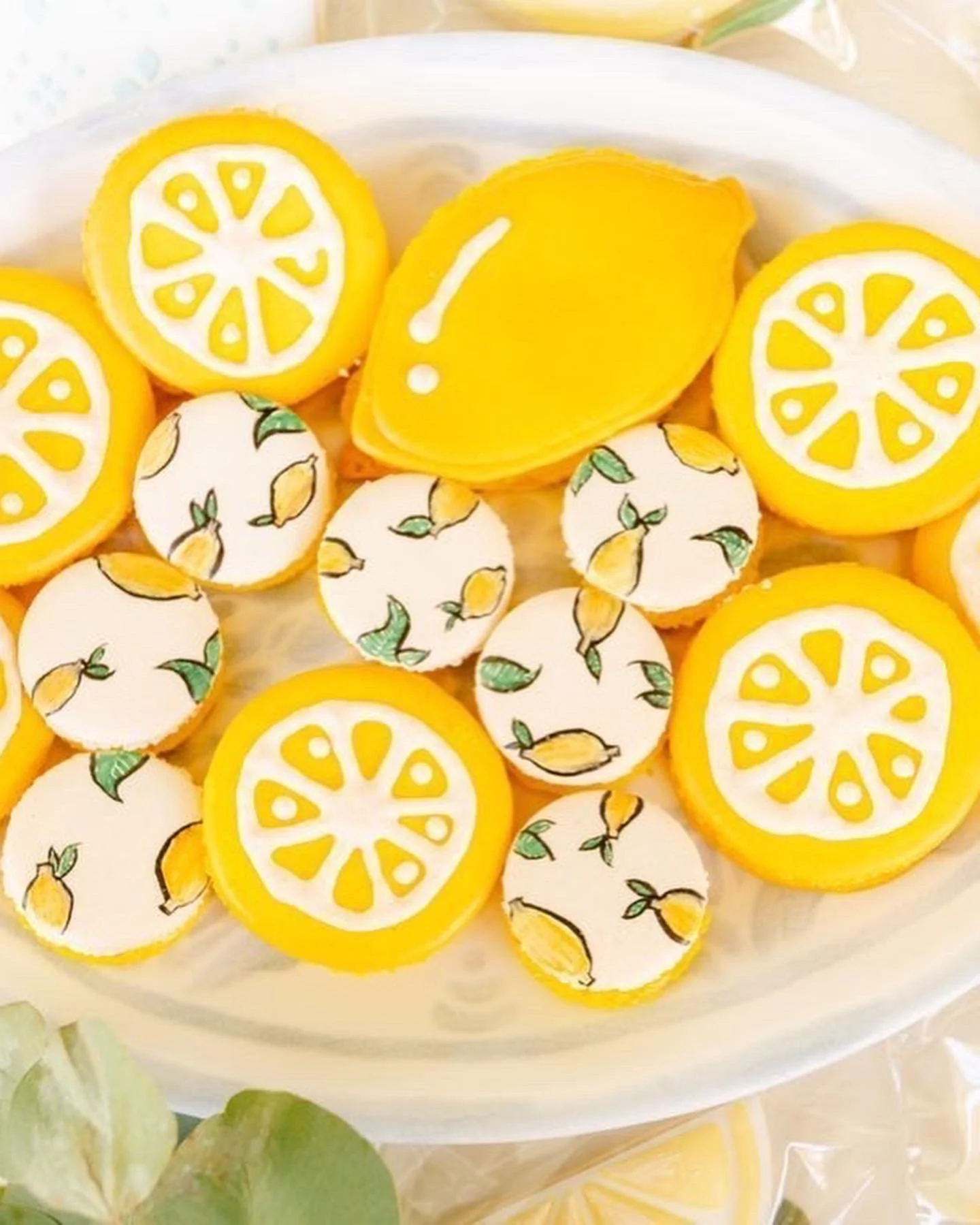 Assorted lemon-themed cookies with yellow and white icing, some with lemon slice designs and others with lemon illustrations, arranged on a platter — handcrafted macarons and desserts at Decadent Macaron café in Gilbert, Arizona