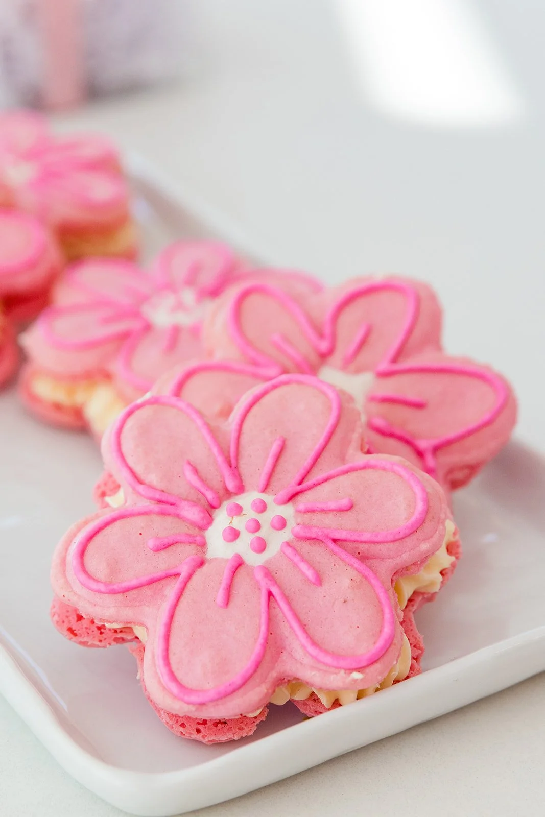 Close-up of pink flower-shaped cookies with piping detail on a white rectangular plate — handcrafted macarons and desserts at Decadent Macaron café in Gilbert, Arizona