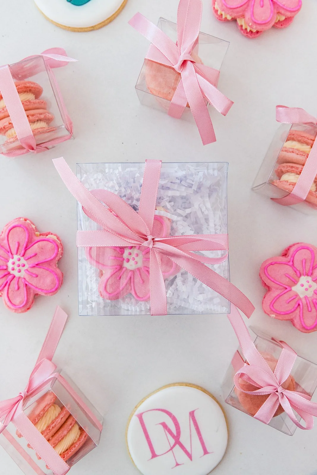 Pink flower-shaped cookies and small gift boxes with pink ribbons, arranged on a white surface — custom dessert catering and events by Decadent Macaron in Gilbert, Arizona