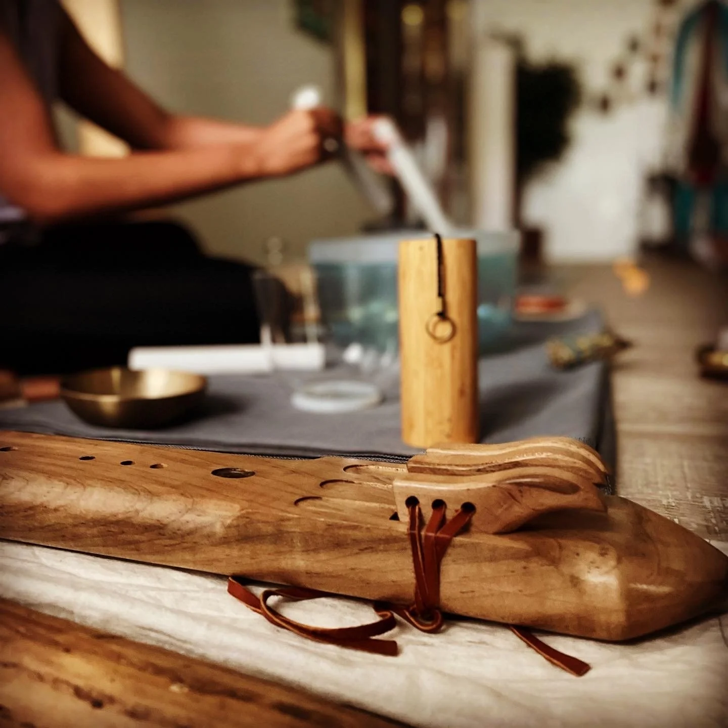 Close-up of a wooden carved object on a table with various small objects and a blurred person in the background.
