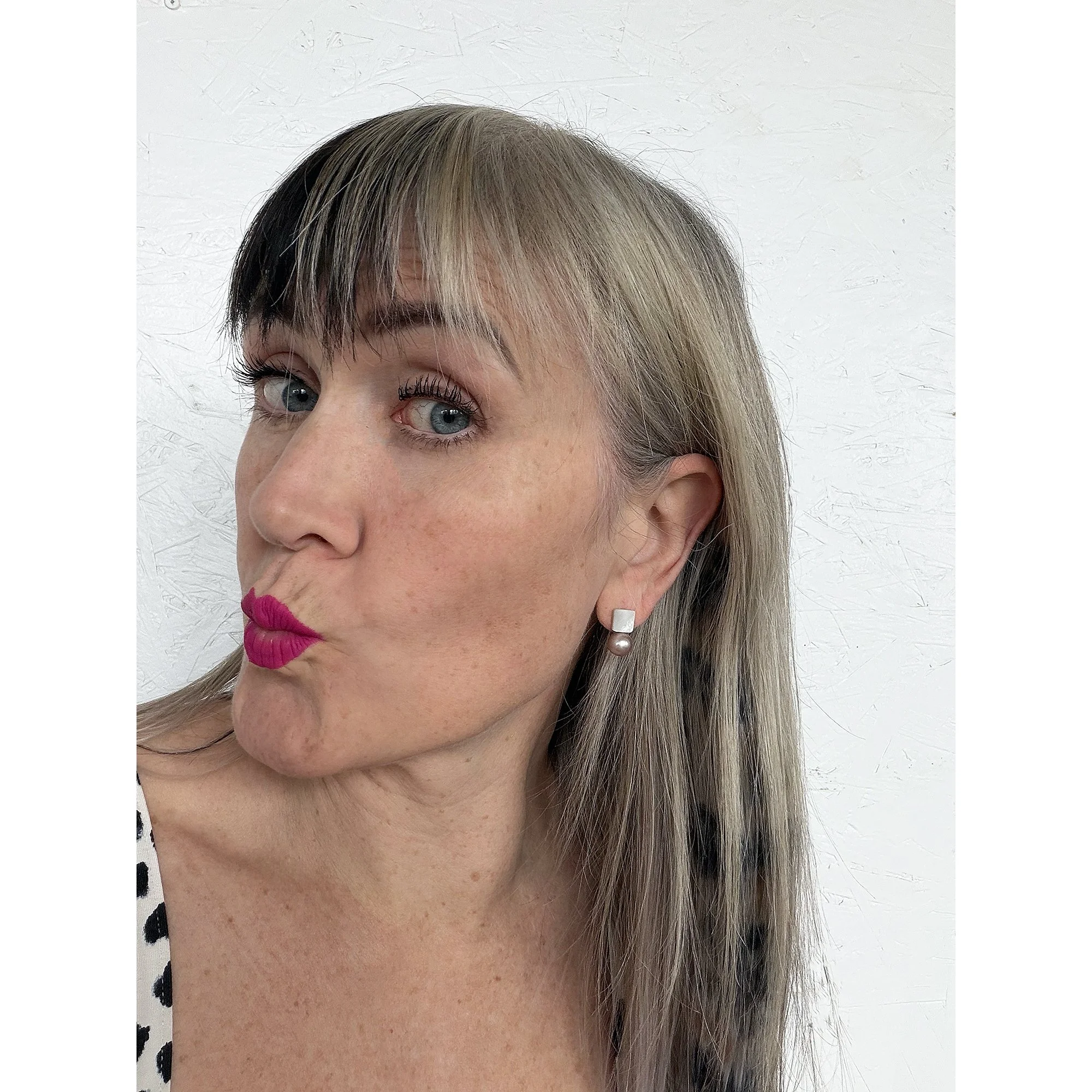woman with blue eyes blonde hair and pink lipstick wearing small earring with shimmery mother of pearl and a big round pink freshwater pearl