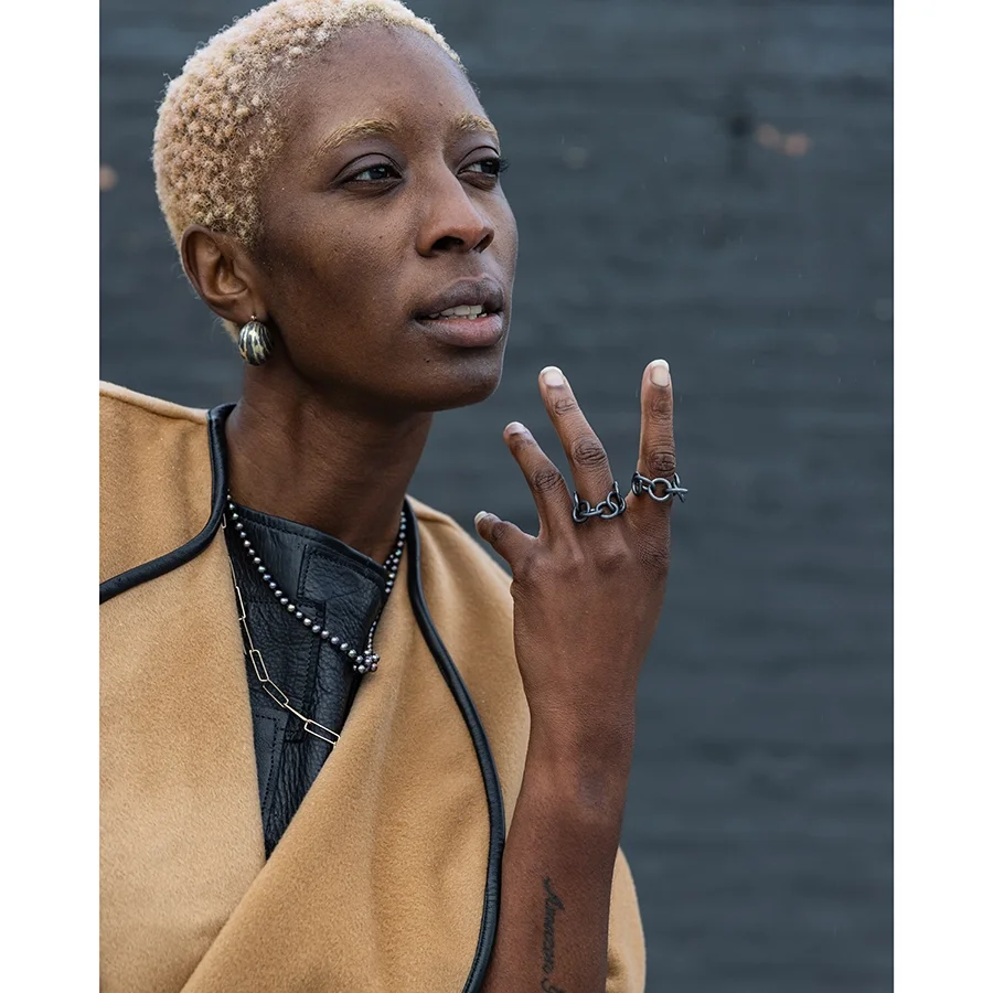 woman with blonde short hair and dark skin wearing a tan trenchcoat and oxidized sterling silver bauble hoop earrings