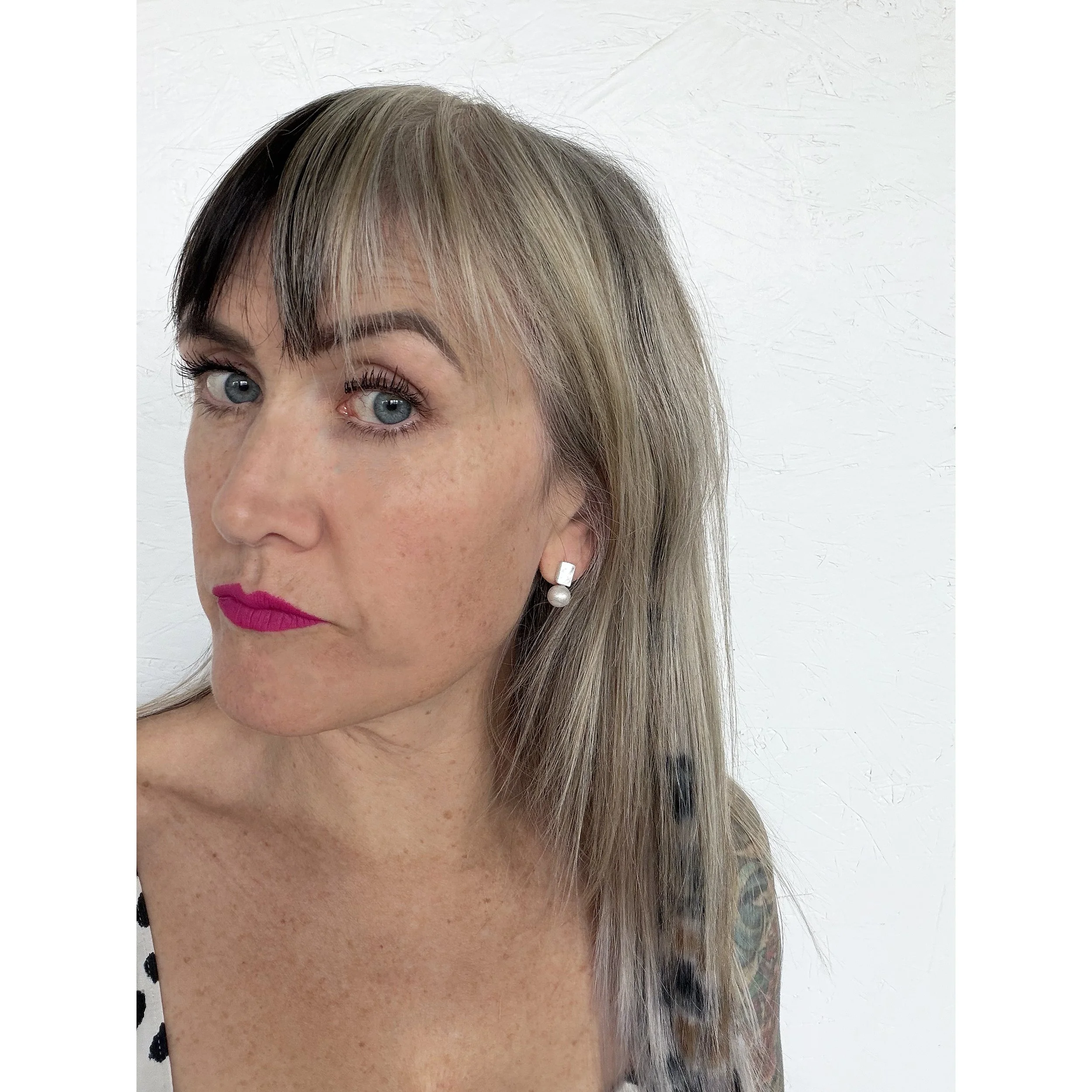 E541b.jpgfront view of woman with blonde hair, pink lipstick and black and white tank top wearing small iridescent mother of pearl earrings with big white freshwater pearl