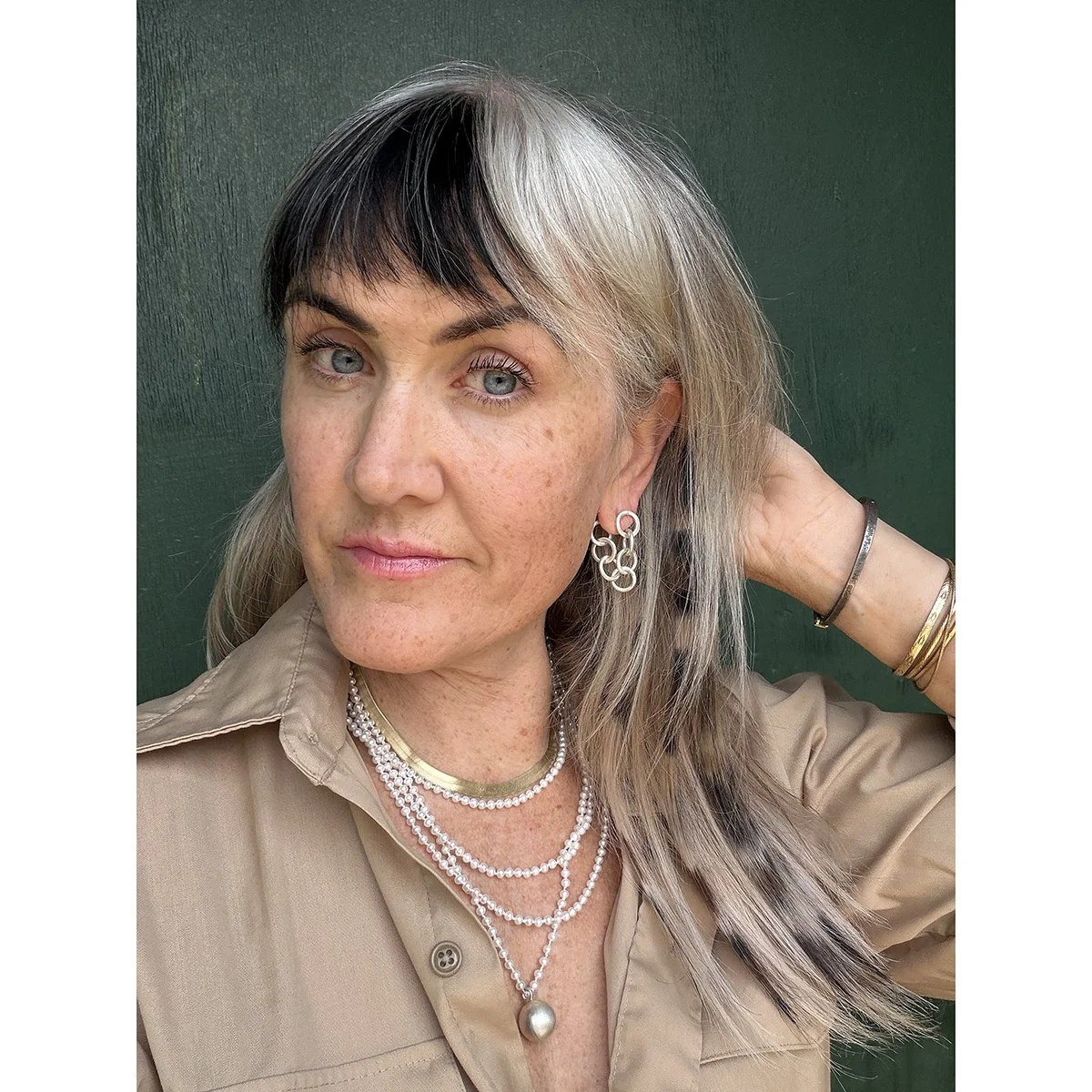 silver chain earrings on woman with blonde and brown hair wearing also pearl necklace and gold chain in front of green wall