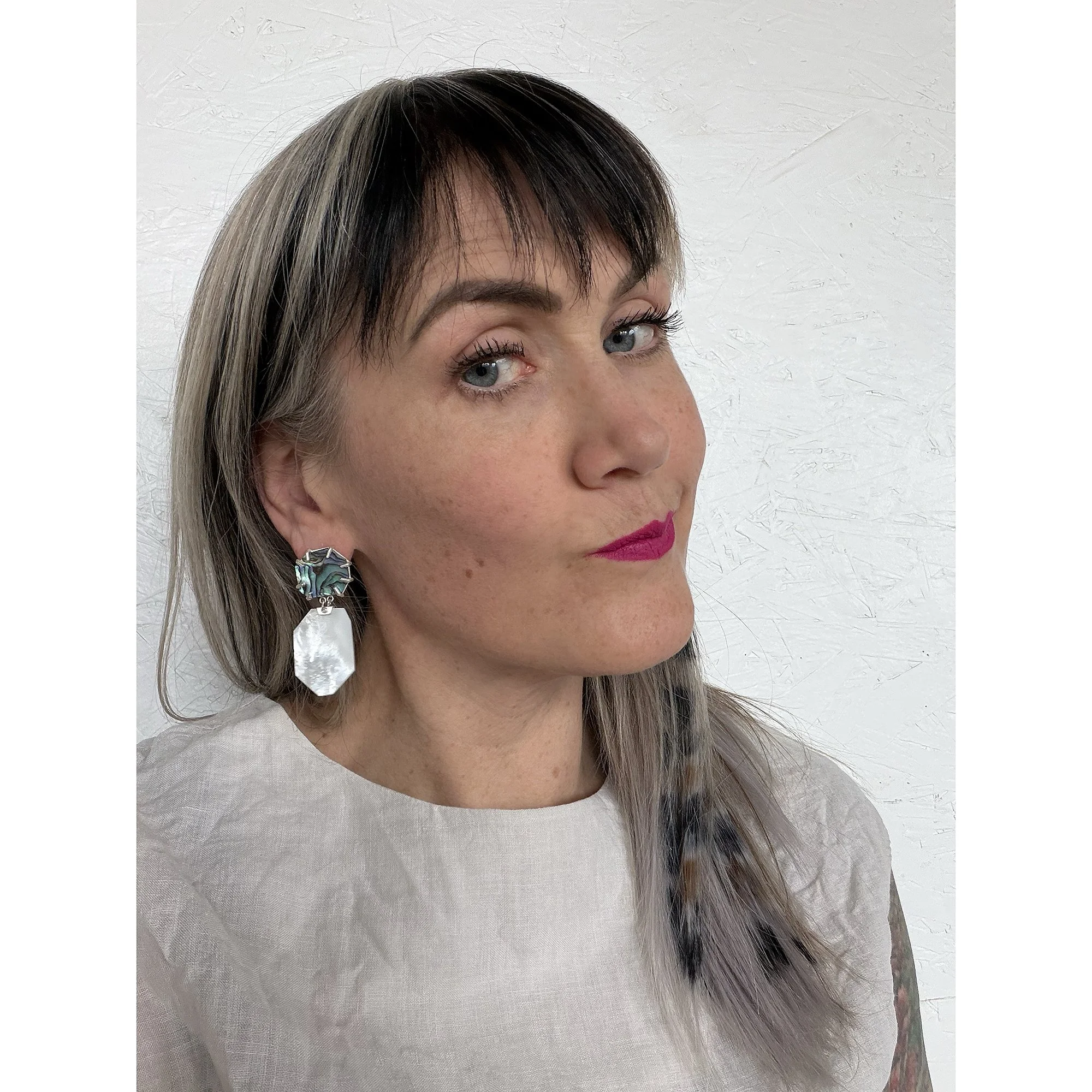 woman with blonde hair and pink lipstick wearing dangling mother of  pearl and green abalone earrings with sterling silver prongs