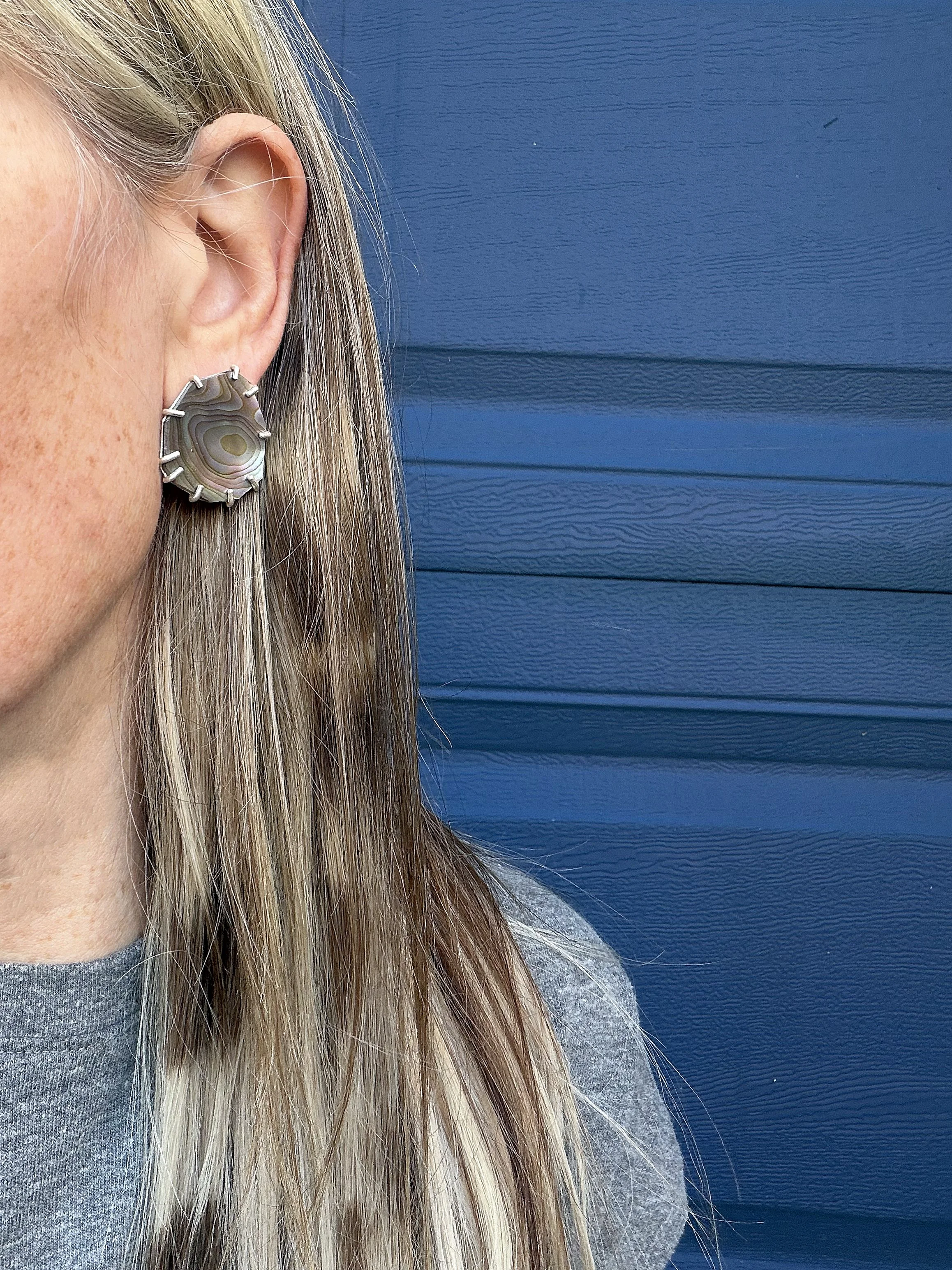 red, purple, pink and green shimmery earrings with sterling silver prongs on a woman's ear wearing a gray shirt with long blonde hair