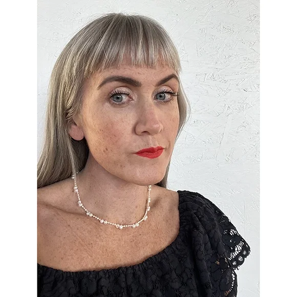 small freshwater pearl necklace with small and medium sized alternating white pearls on a woman with a dark blue lace top, freckles and blonde hair in front of a white background