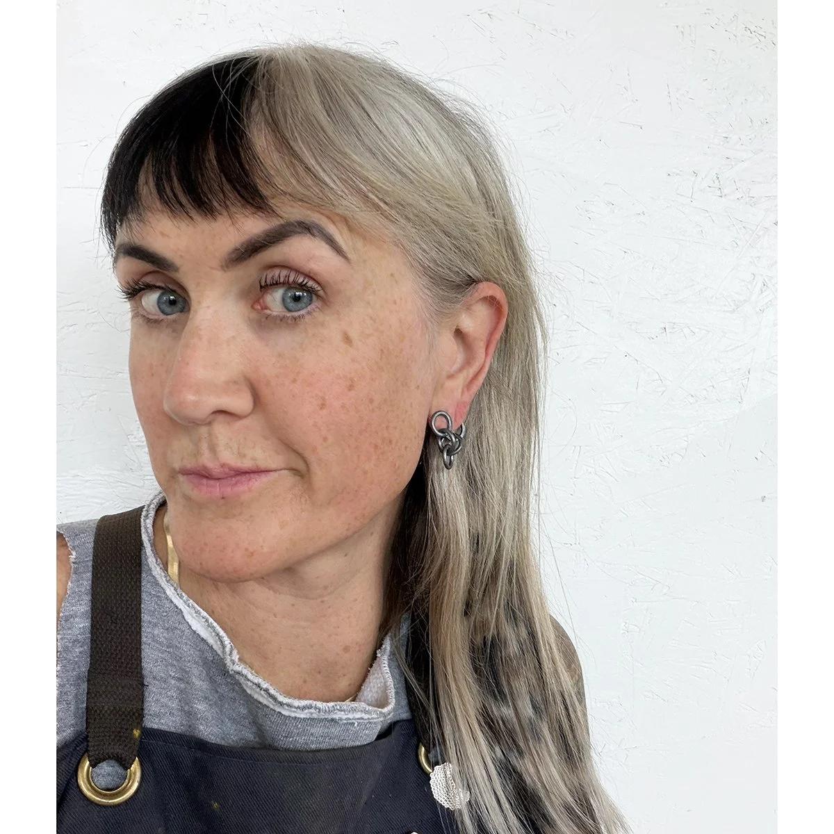 small dark black chain earrings on blonde woman with freckles again white wall