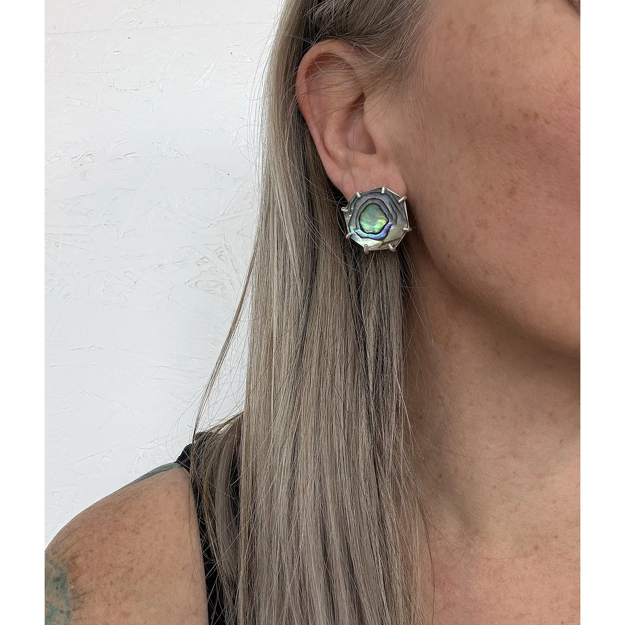a close up view of green, purple and blue shiny swirl abalone post earrings with silver prongs