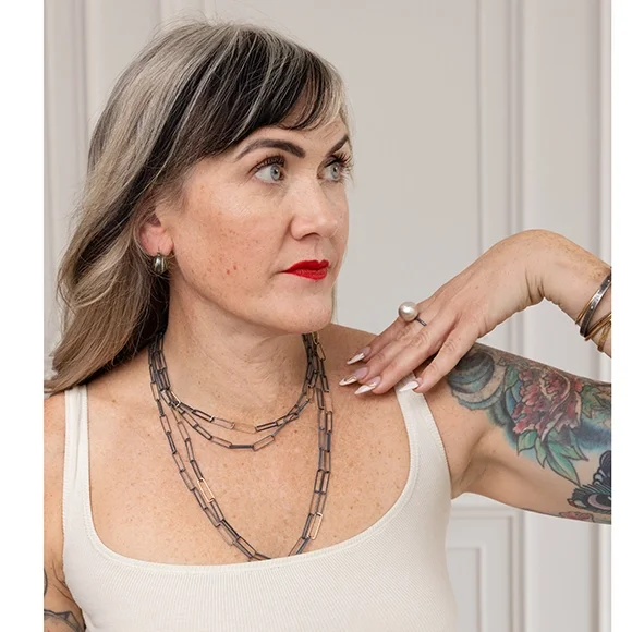 small dark and gold bauble earrings on woman with black and white hair, red lipstick and wearing long and short black necklaces