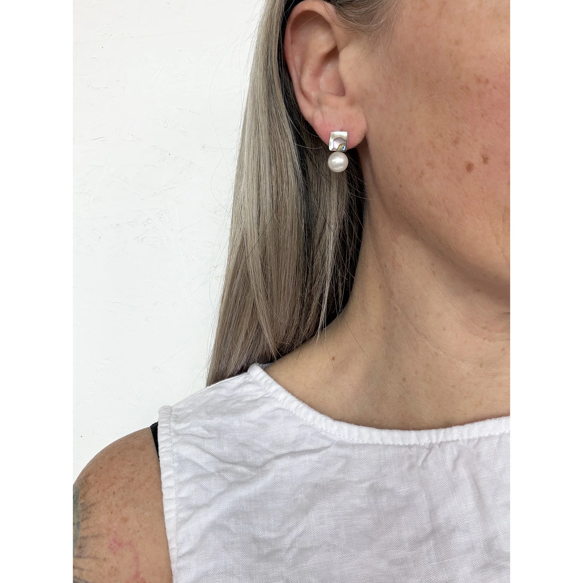 side view of woman with blonde hair and freckles wearing small pearl and abalone earring close up of earring