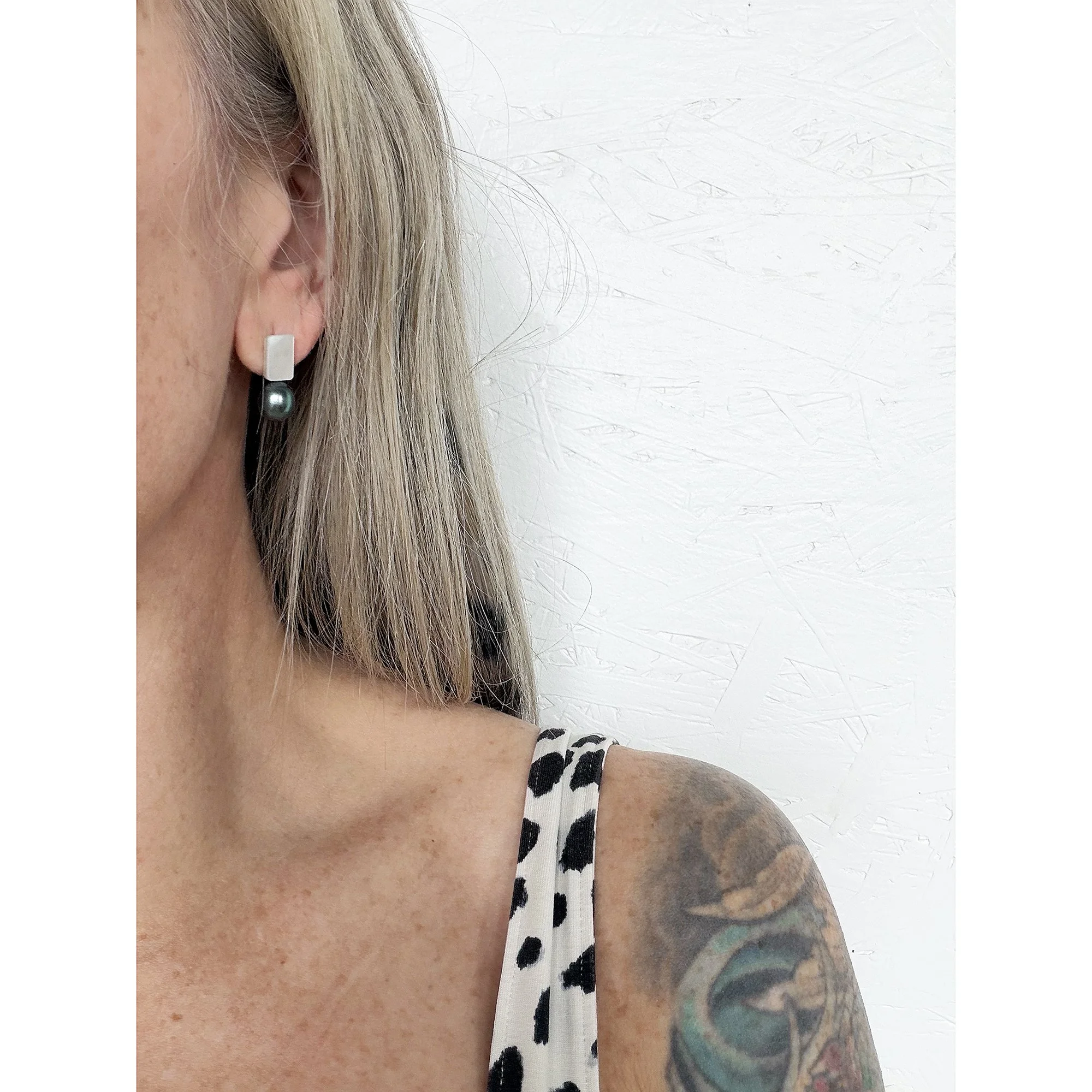 close up of woman’s ear with blonde hair and round deep blue black and green freshwater pearl next to iridescent mother of pearl chunk