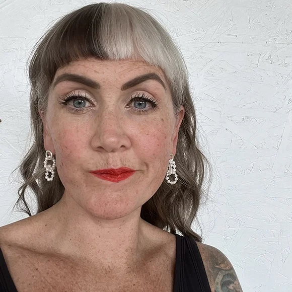 small white pearl earrings on woman with freckles bright blue eyes and red lips wearing black tee shirt and white background
