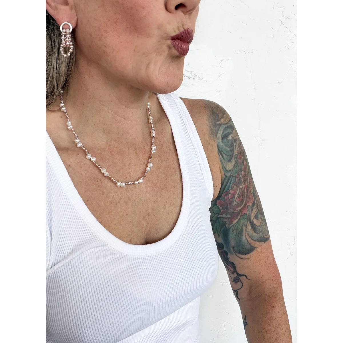 woman wearing small pink freshwater pearl earrings and pink and white pearl necklace and white tank top