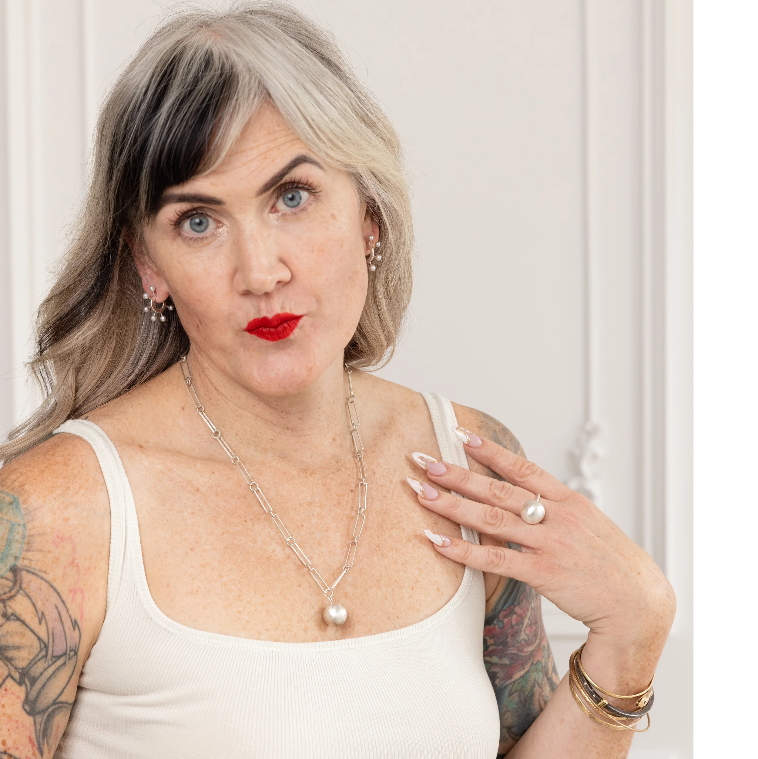 woman wearing single silver ring single silver necklace with handmade chain and two sets of earrings with blonde hair, red lips and in front of textured background