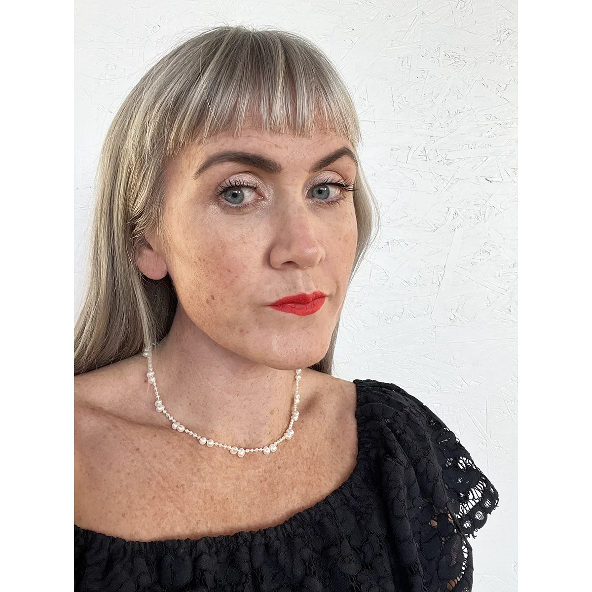 small freshwater pearl necklace with small and medium sized alternating white pearls on a woman with a dark blue lace top, freckles and blonde hair in front of a white background