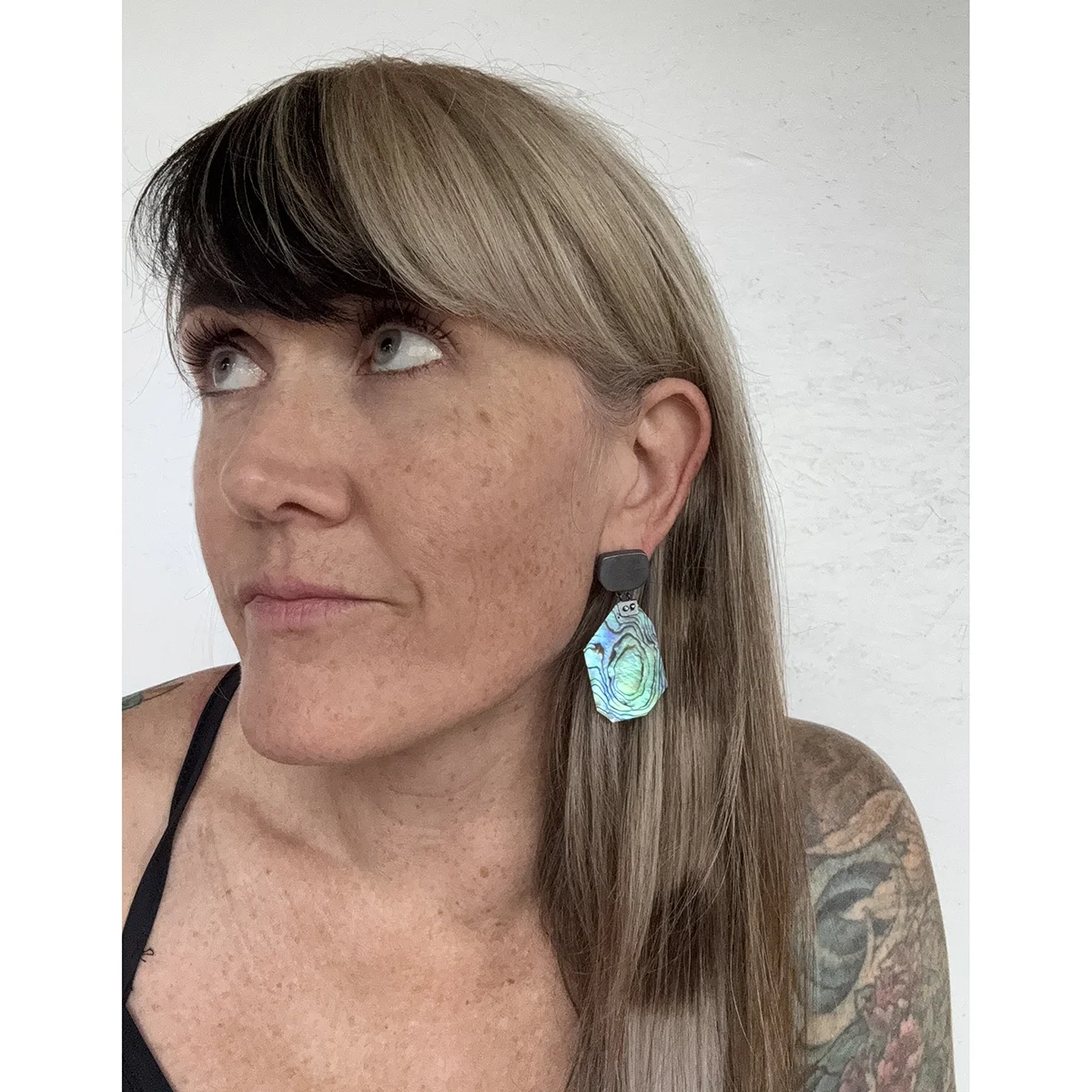 woman wearing bright green irridescent earring with blonde hair and tank top