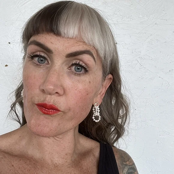 small white pearl earrings on woman with freckles bright blue eyes and red lips wearing black tee shirt and white background