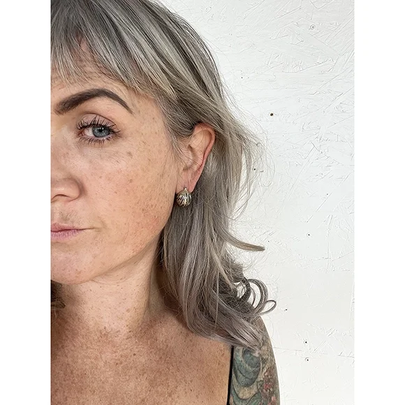 small yellow gold and sterling silver earrings on woman with blonde hair and freckles wearing brown tank top in front of white background