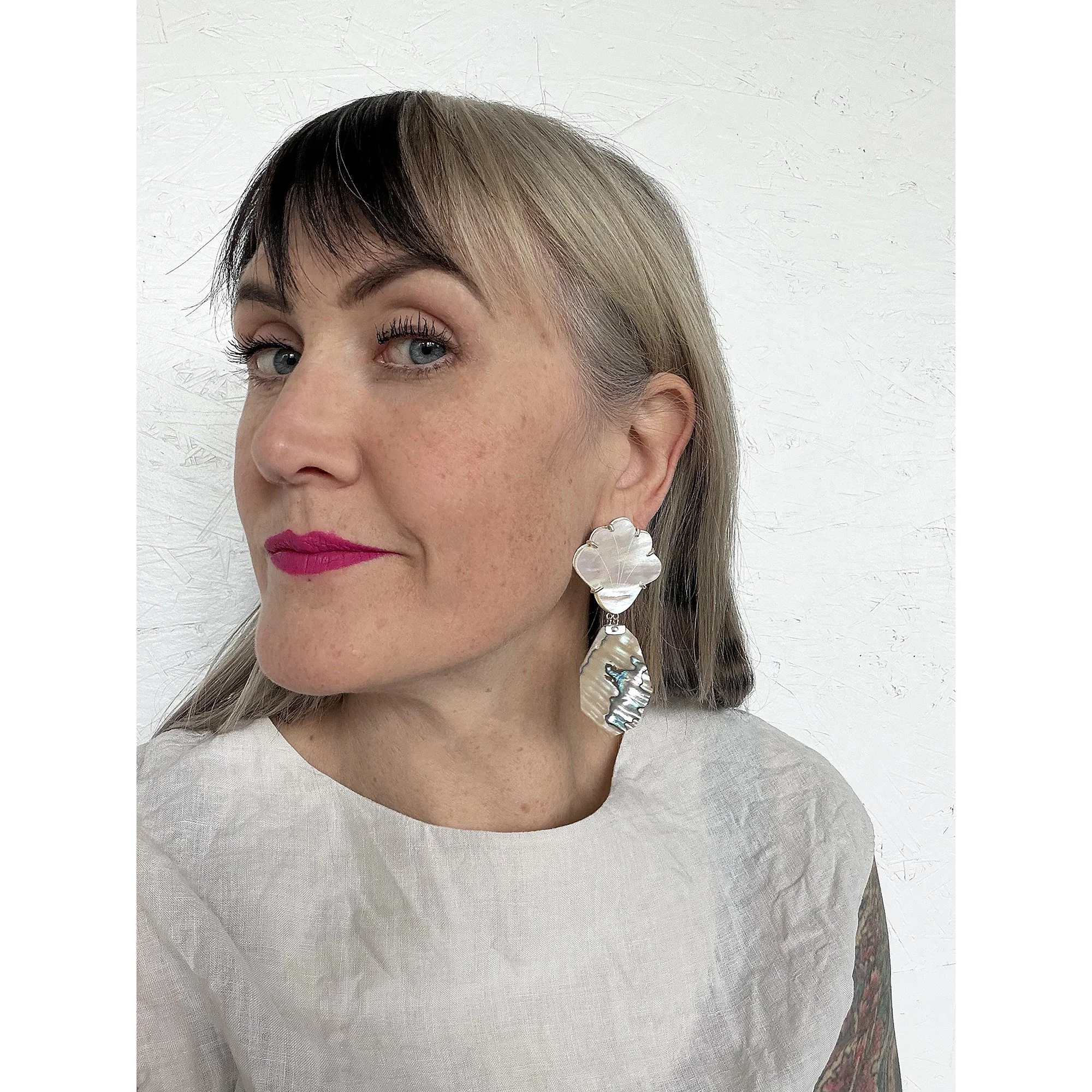 woman with blonde hair and pink lipstick wearing large flashy pearl earrings