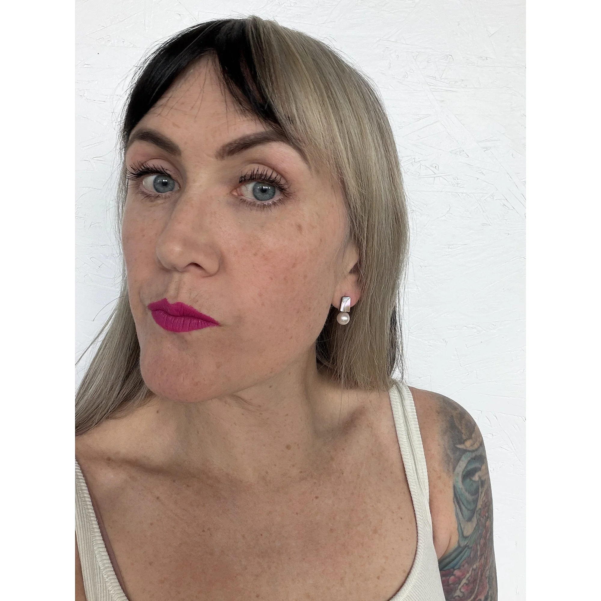 front view of woman with blonde hair, pink lipstick and black and white tank top wearing small iridescent mother of pearl earrings with big white freshwater pearl