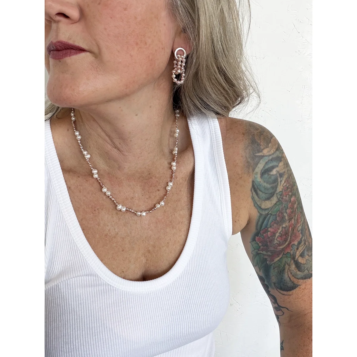 woman wearing small pink freshwater pearl earrings and pink and white pearl necklace and white tank top