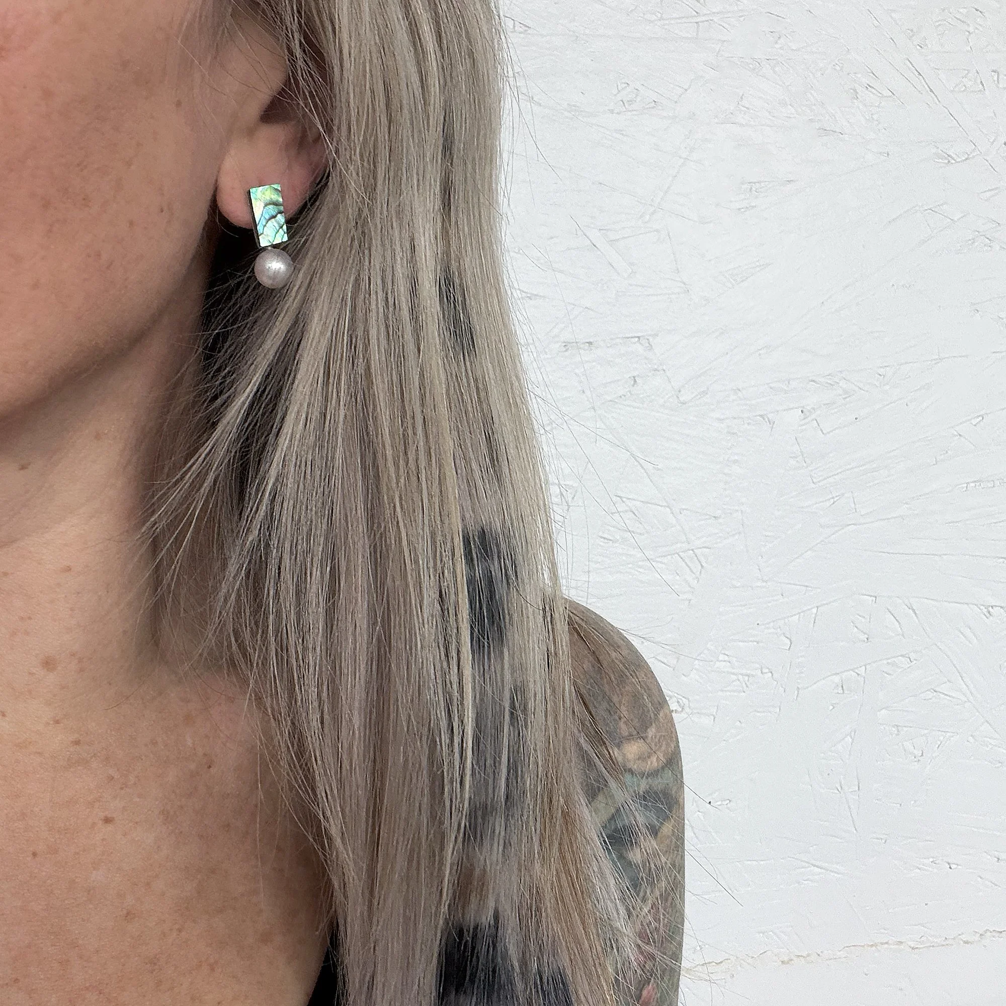 close up of woman’s ear with blonde hair and dark green abalone shell small earring and round perfect white pearl
