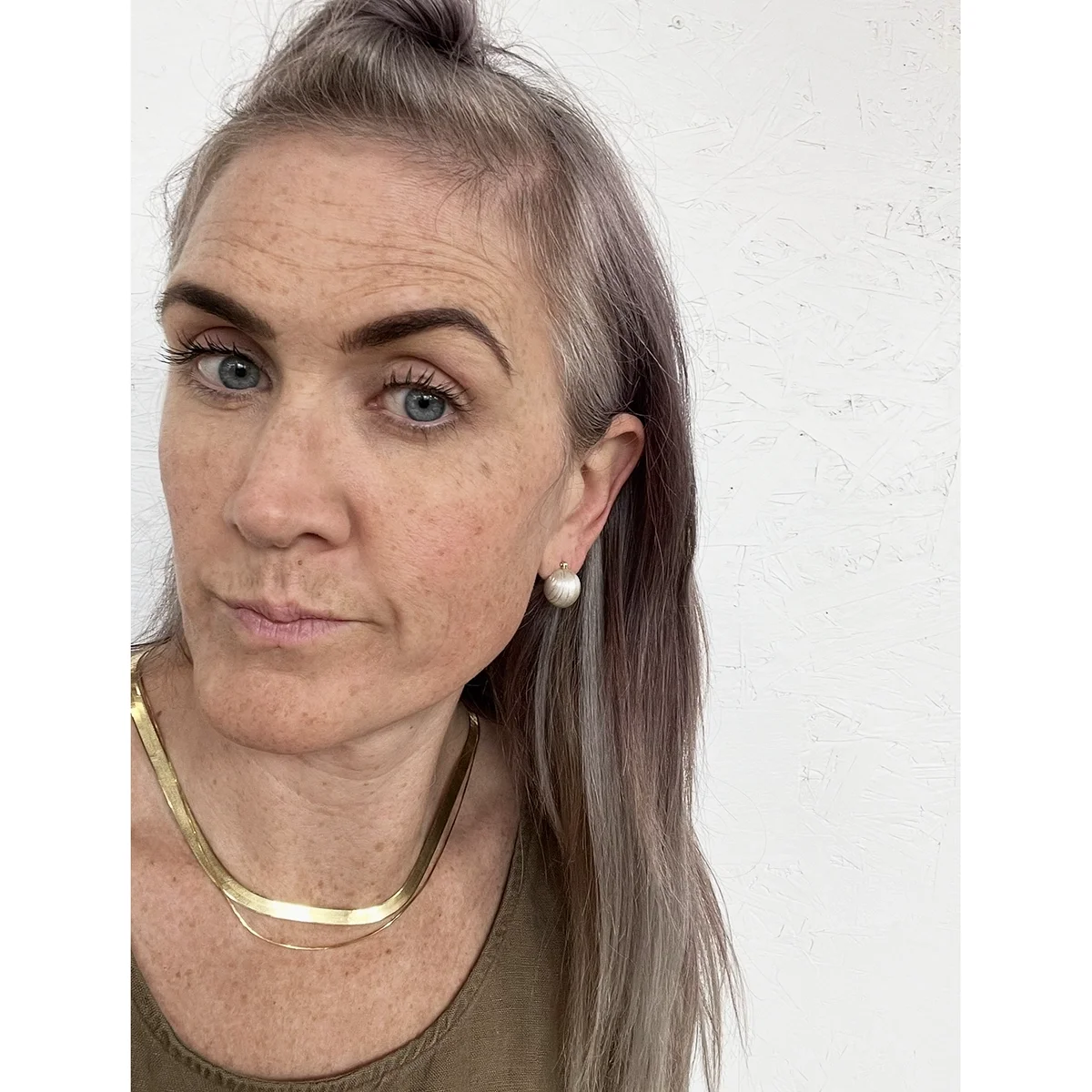 woman with blond hair and tan tank top wearing small shiny sterling silver ball earrings and two gold chains