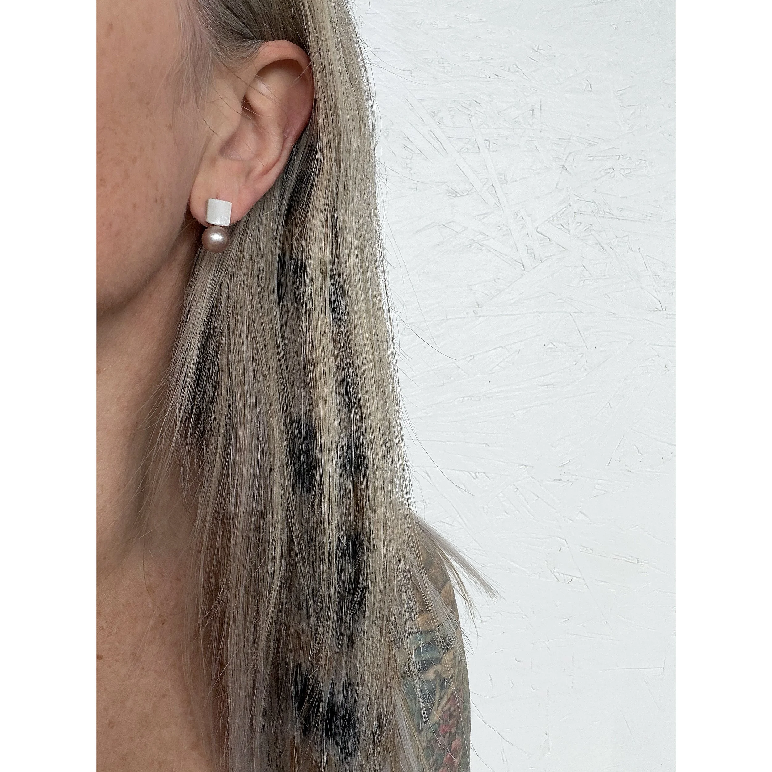 close up of woman’s ear with blonde hair and big pink freshwater pearl next to iridescent mother of pearl hand shaped squares