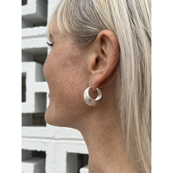 sterling silver hoop earrings on woman with blond hair, freckles and white tank top in front of white bricks with unique cut out design