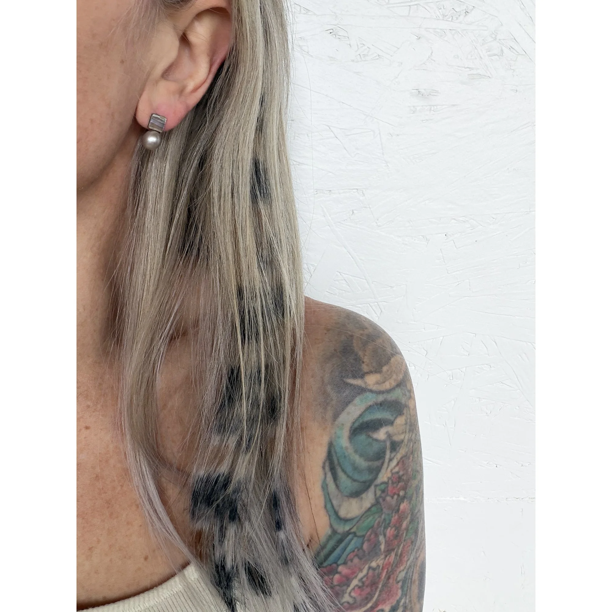 side view of woman with blonde hair, freckles and tattoos wearing small silver pearl and red abalone post earring with purples pinks and blues