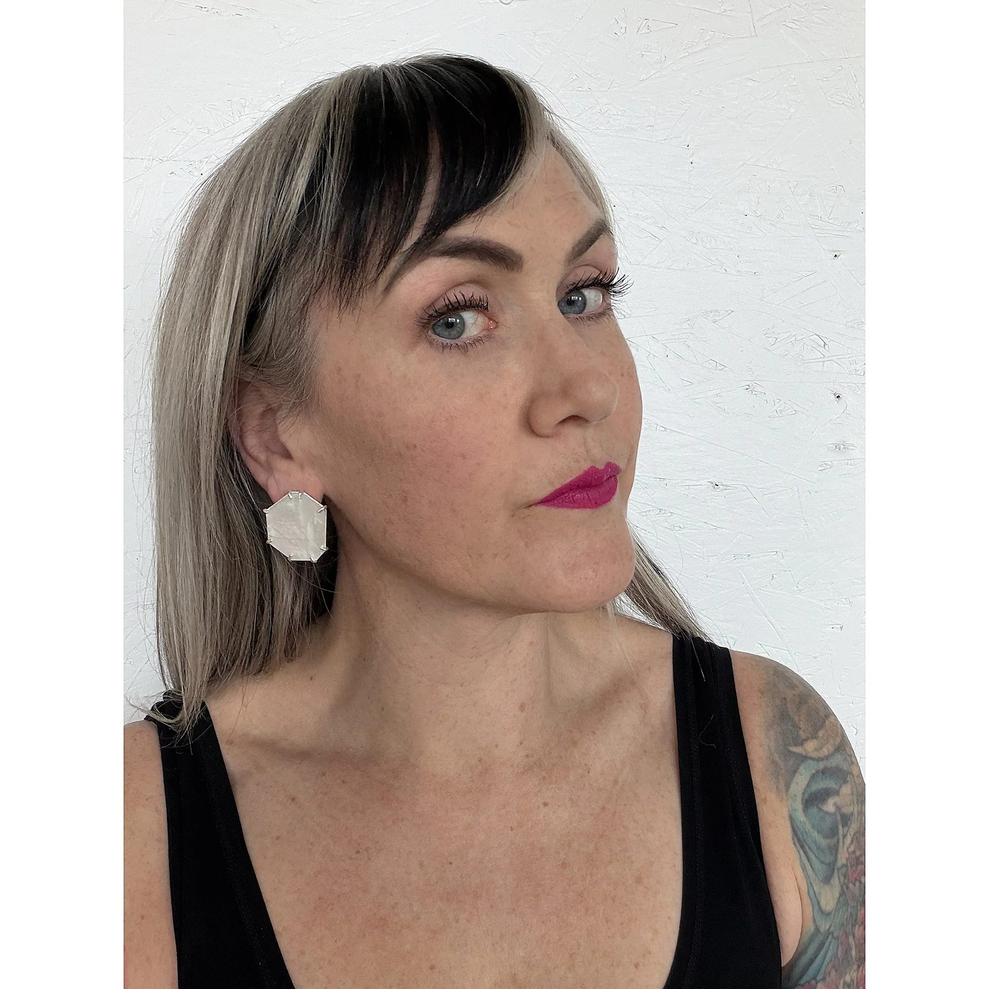 Blonde woman with pink lipstick wearing white mother of pearl post earrings and black tank top