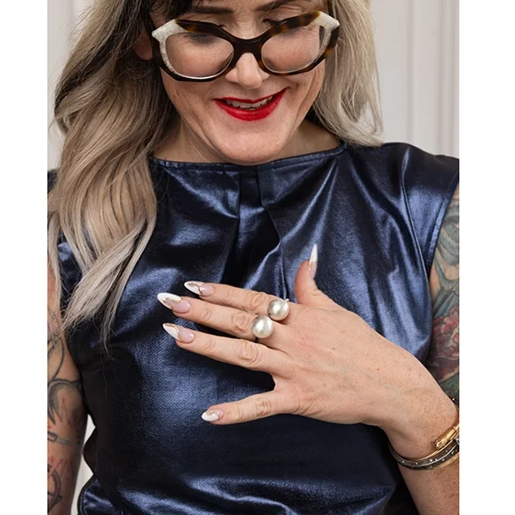 woman wearing two silver ball rings wearing big frame tortishell glasses and blue shimmery top