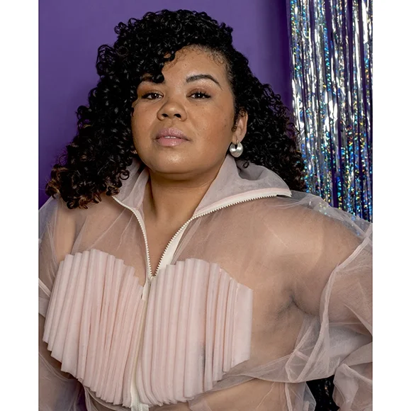 bright silver earrings on woman with dark curly hair wearing pink ruffle top in front of purple and reflective silver shimmer background