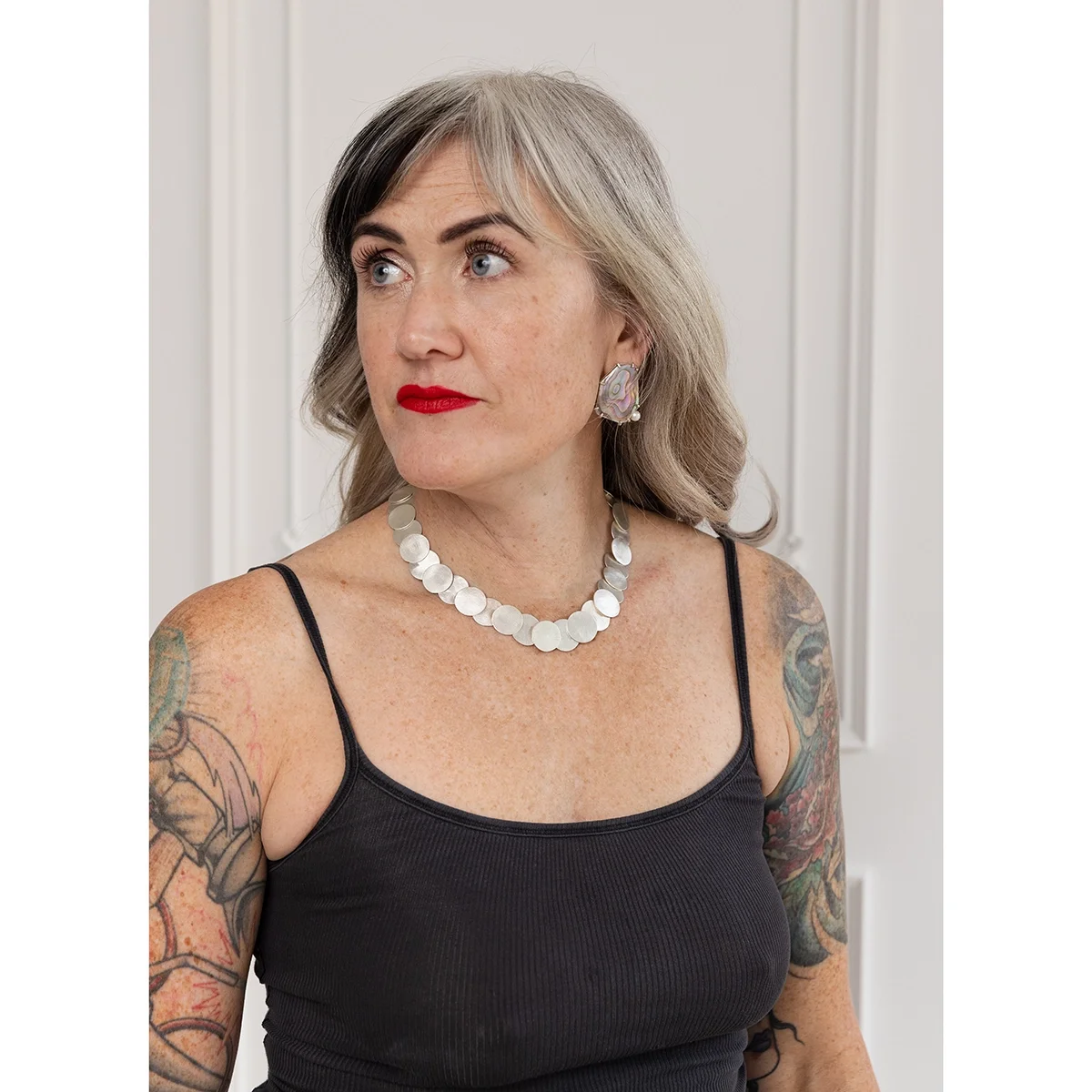 woman with blonde hair and red lips wearing geometric pink and green abalone earrings in front of white textured wall