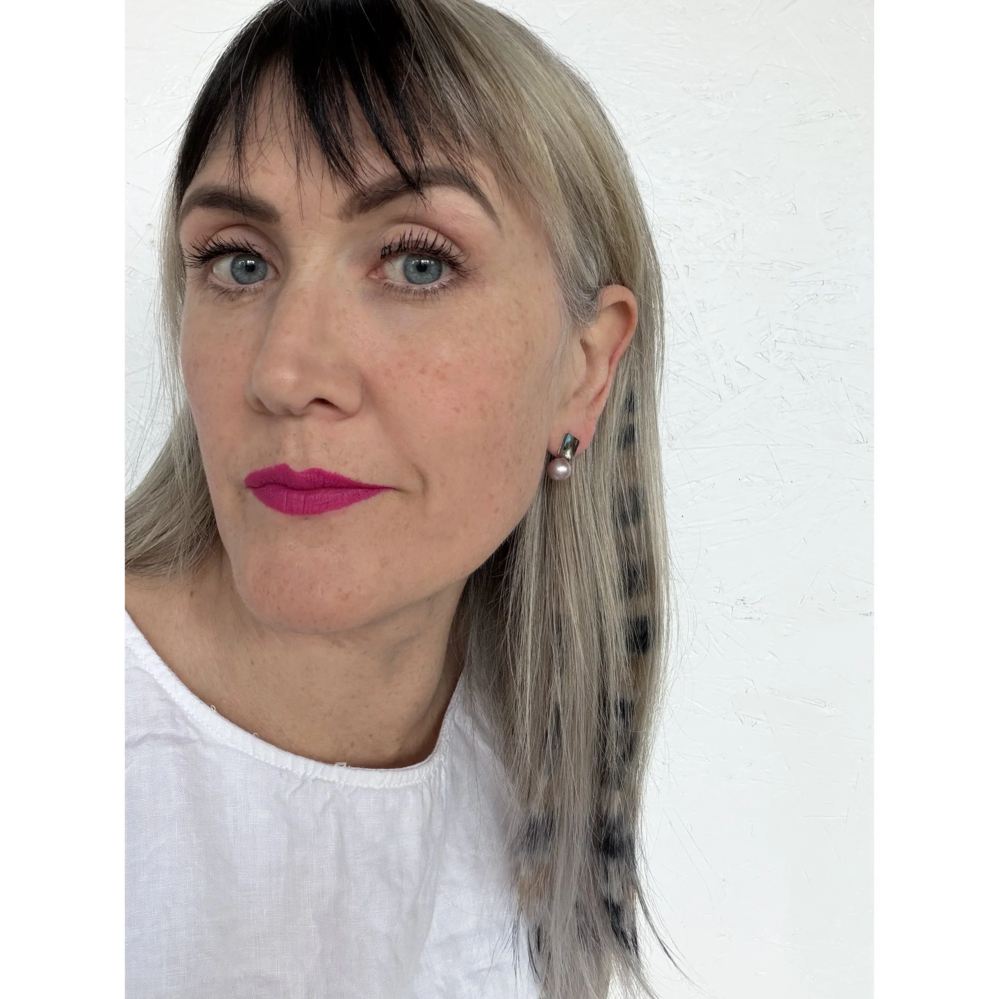 woman with blue eyes blonde hair and pink lipstick wearing colorful pearl and shell earrings