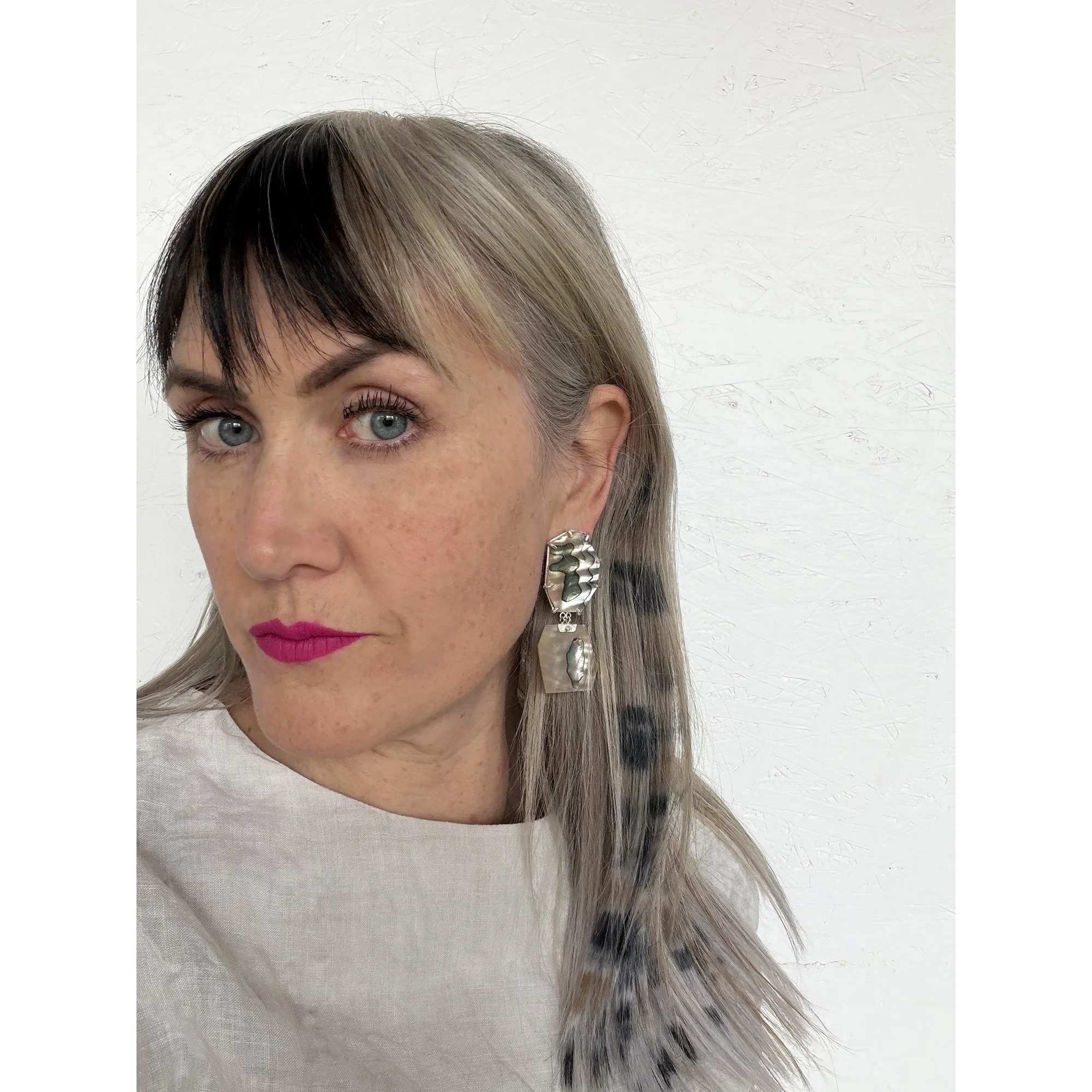 a beautiful woman with blonde and brown striped hair and pink lipstick wearing shiny earrings