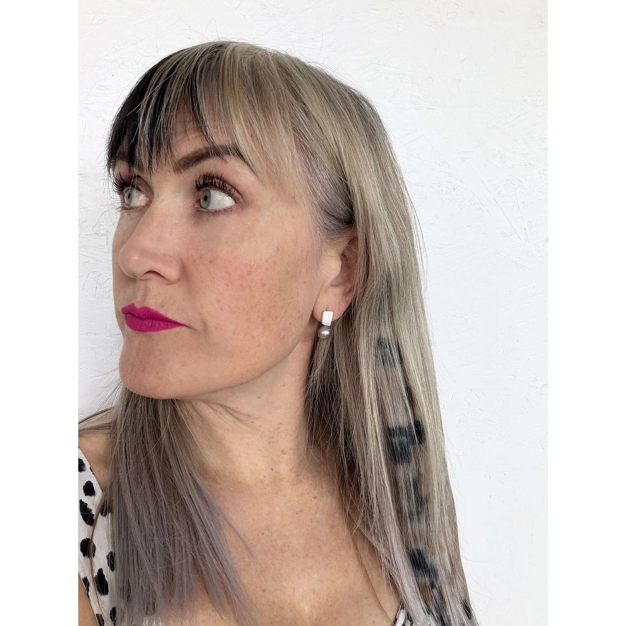 front view of woman with blonde hair, pink lipstick and a black and white shirt wearing small silver pearl and mother of pearl earrings