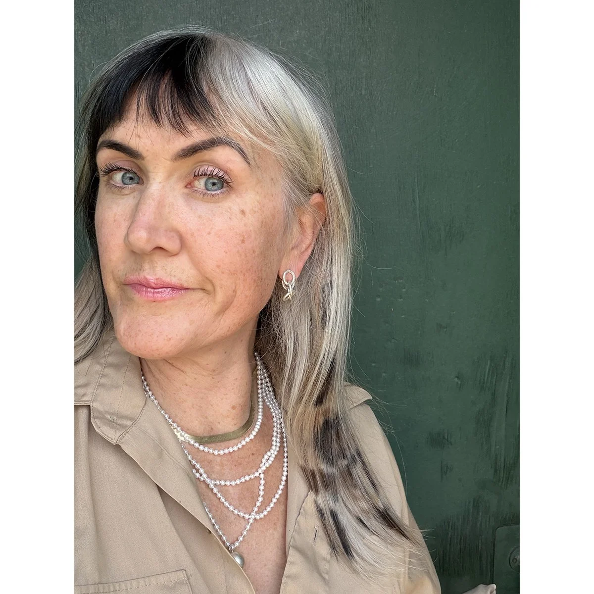 small satin finish silver chain earrings on woman wearing pearl necklace and gold chain in front of green industrial building