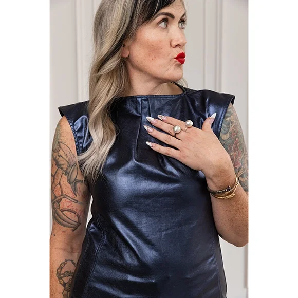 woman with wavy hair, red lips and a blue shimmery long shirt wearing two pearl ball rings and making a kissy face with red lips