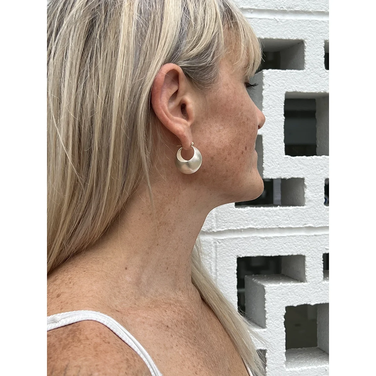 woman with straight blond hair and bangs wearing sterling silver bauble hoop earrings in front of white and black bricks