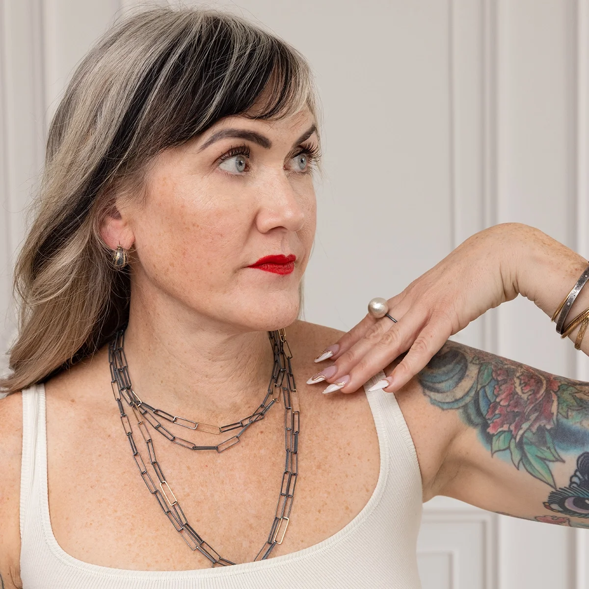 small dark and gold bauble earrings on woman with black and white hair, red lipstick and wearing long and short black necklaces