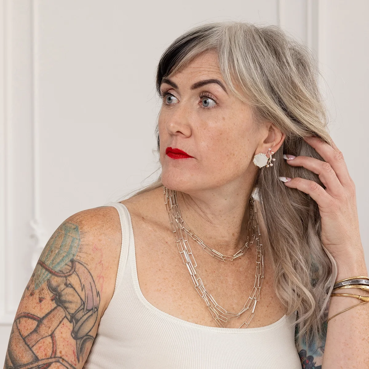 woman with blond hair red lips and arm tattoos wearing pink pearl hoop earrings and multiple sterling silver chain necklaces