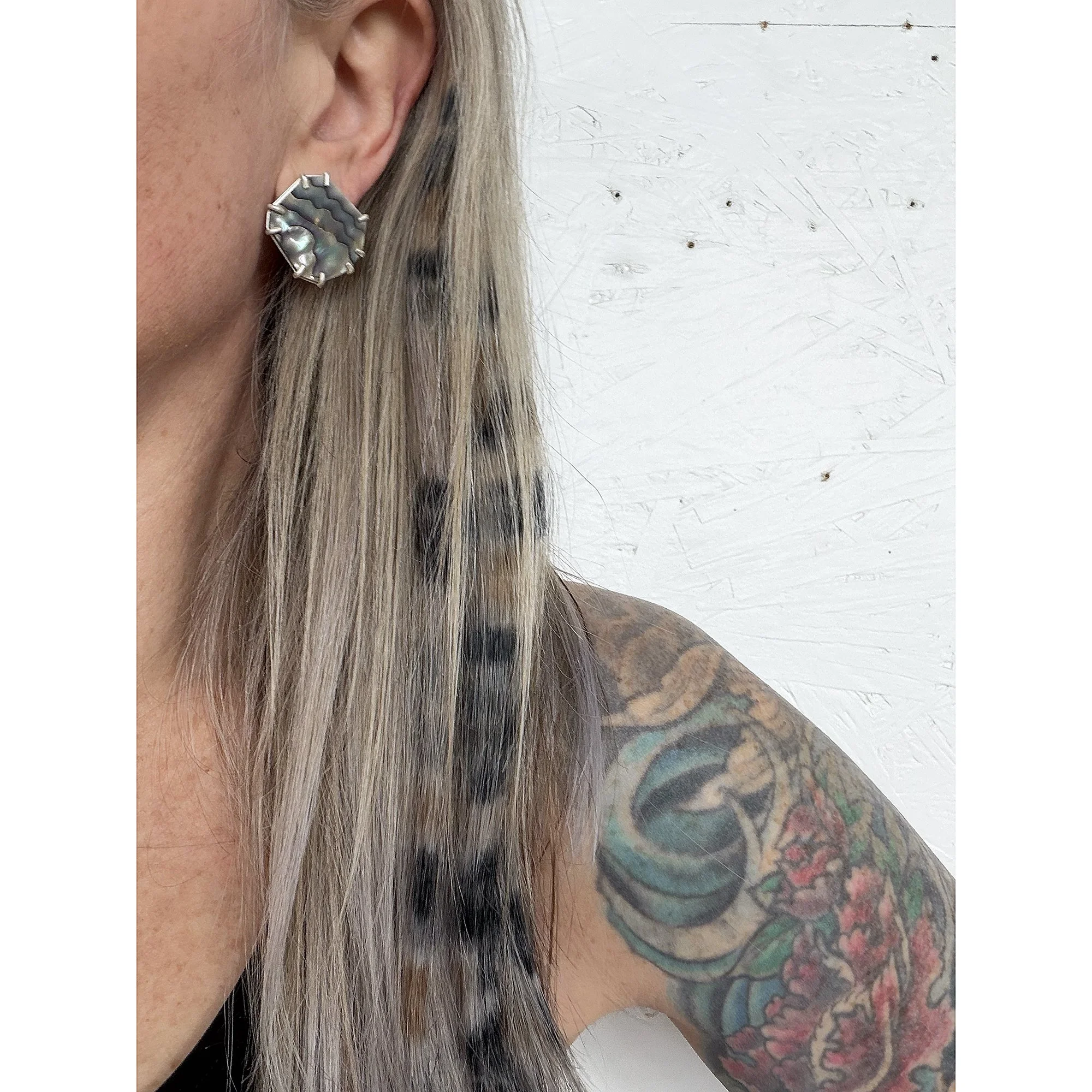 blonde woman wearing patterned abalone earrings with long hair and tattoos