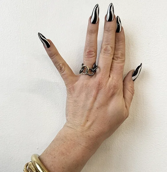 close up of oxidized sterling silver chain ring on hand with long black and white fingernails and several yellow gold bangles on wrist