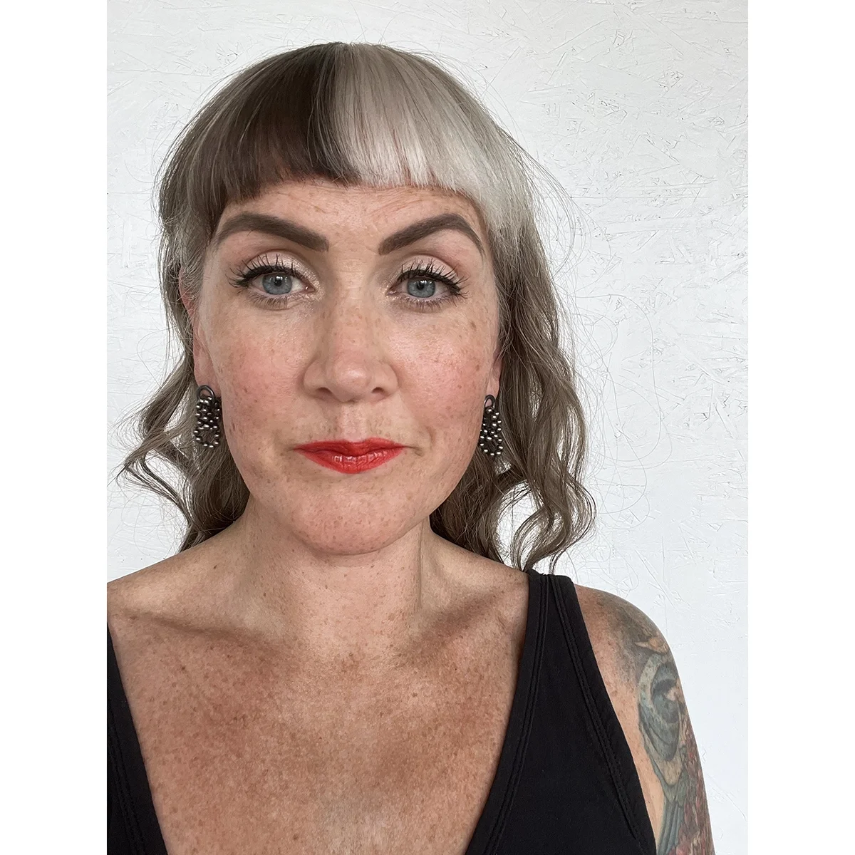 woman with black top, red lips and light hair wearing shiny black pearl earrings