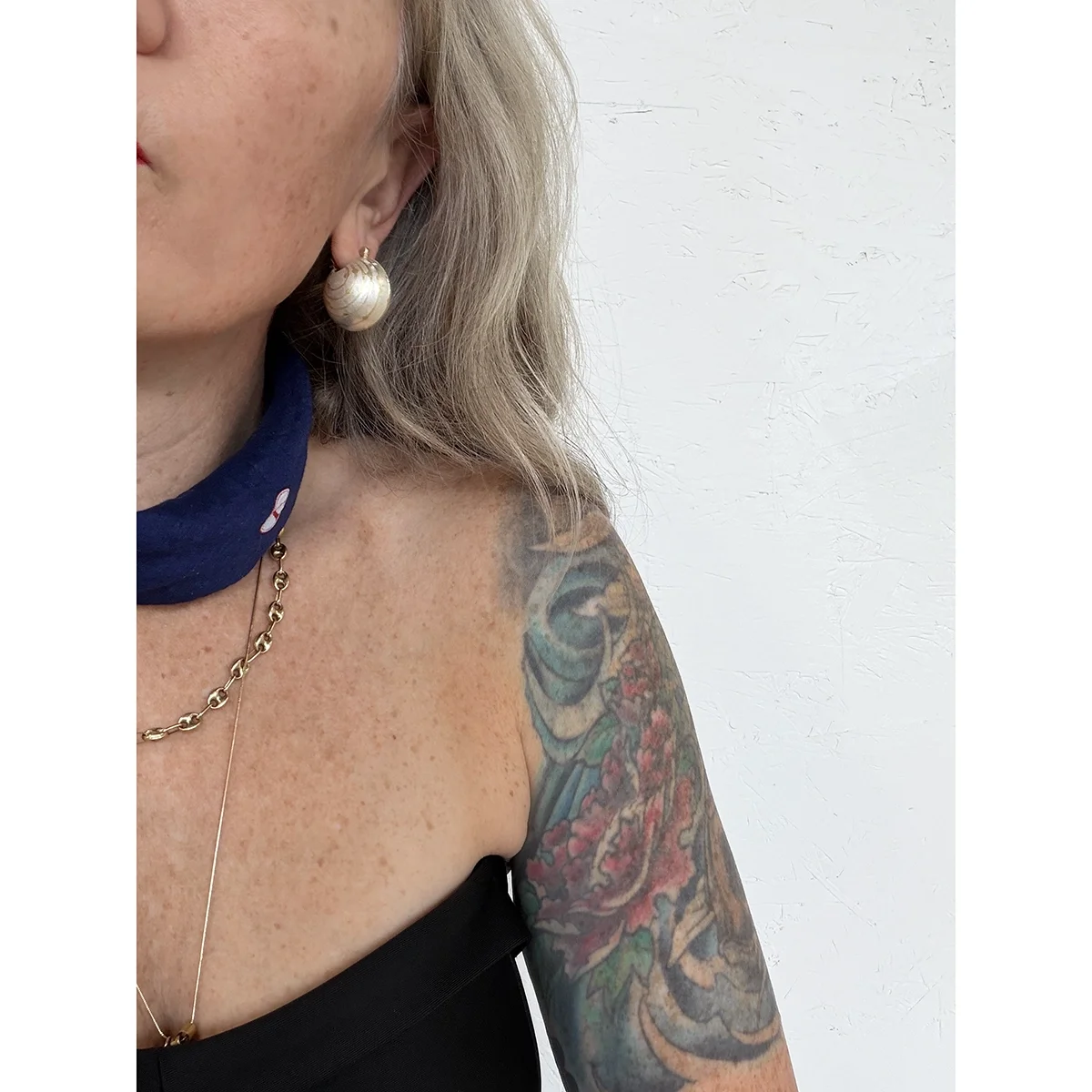 close up of woman with blonde wavy hair, blue eyes, a black strapless top and a blue scarf wearing sterling silver ball earrings with 18k yellow gold lines