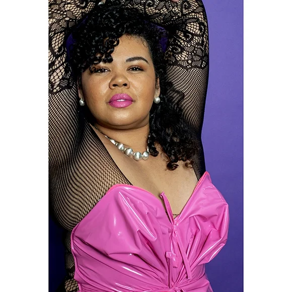 woman with dark curly hair pink corset and black lace top wearing small shiny sterling silver ball earrings in front of dark purple wall