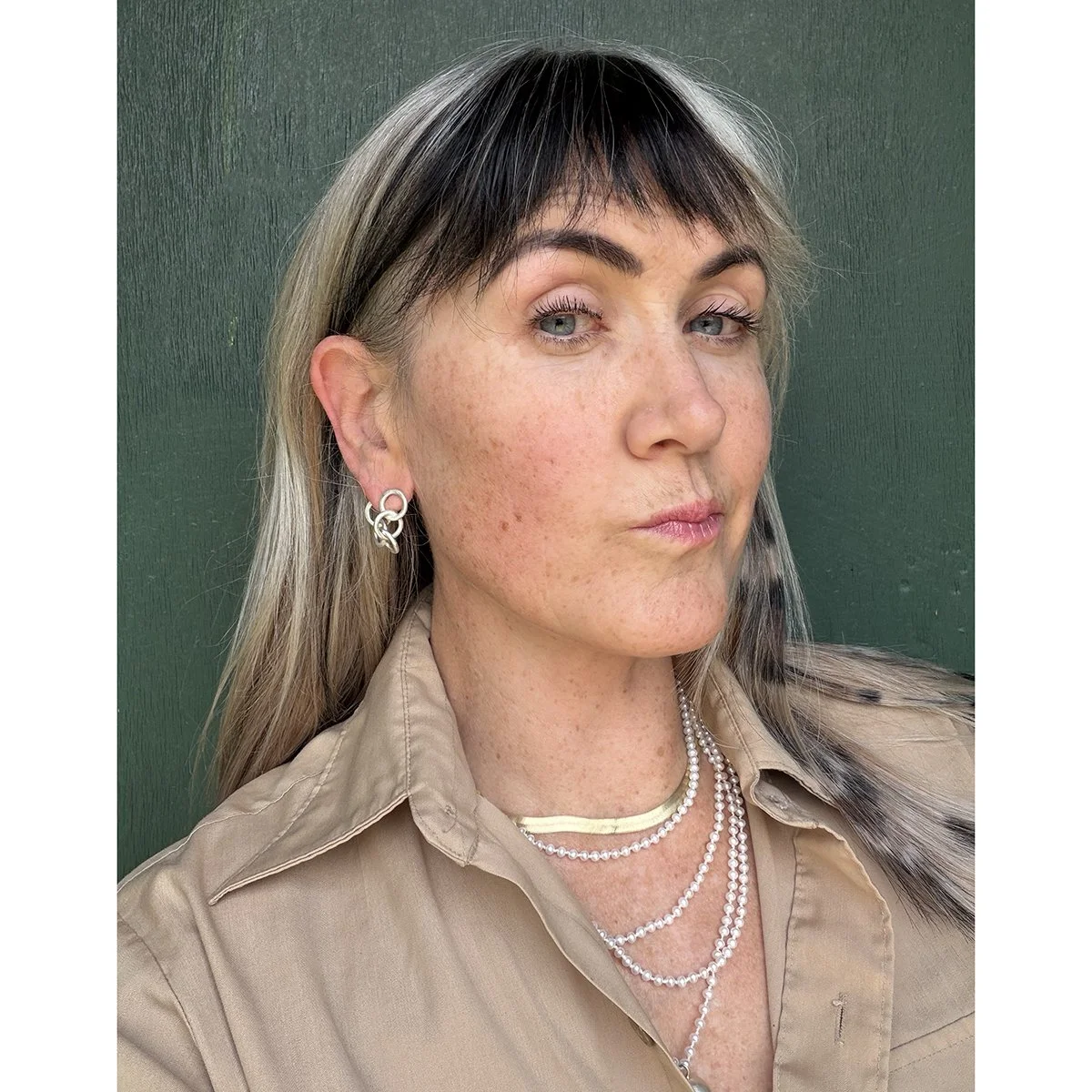 small silver chain earrings on woman with blonde and black hair with green background and pearl necklace